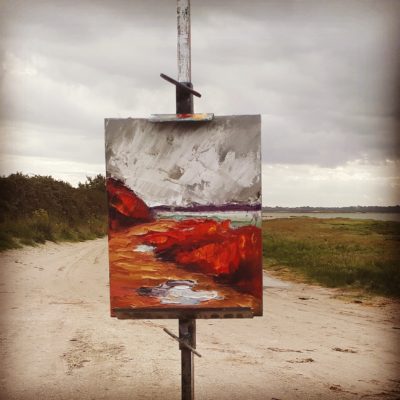 a just completed canvas on the easel beside the sea. and its plain to see that all the greens of the landscape have been replaced by red in the painting.