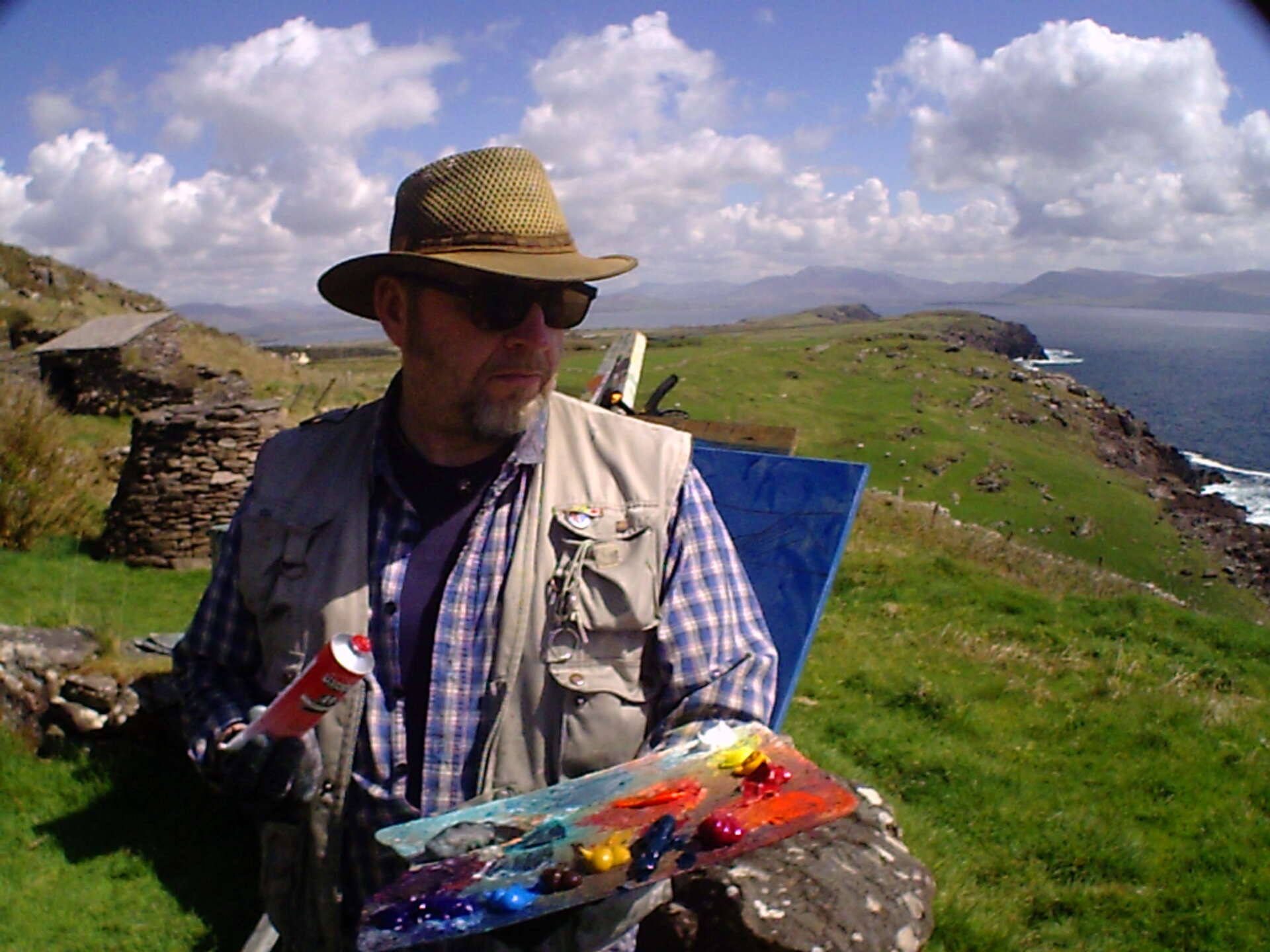 artist rod coyne squeezes extra red paint onto his palette, while working on a clifftop above ballinskelligs bay